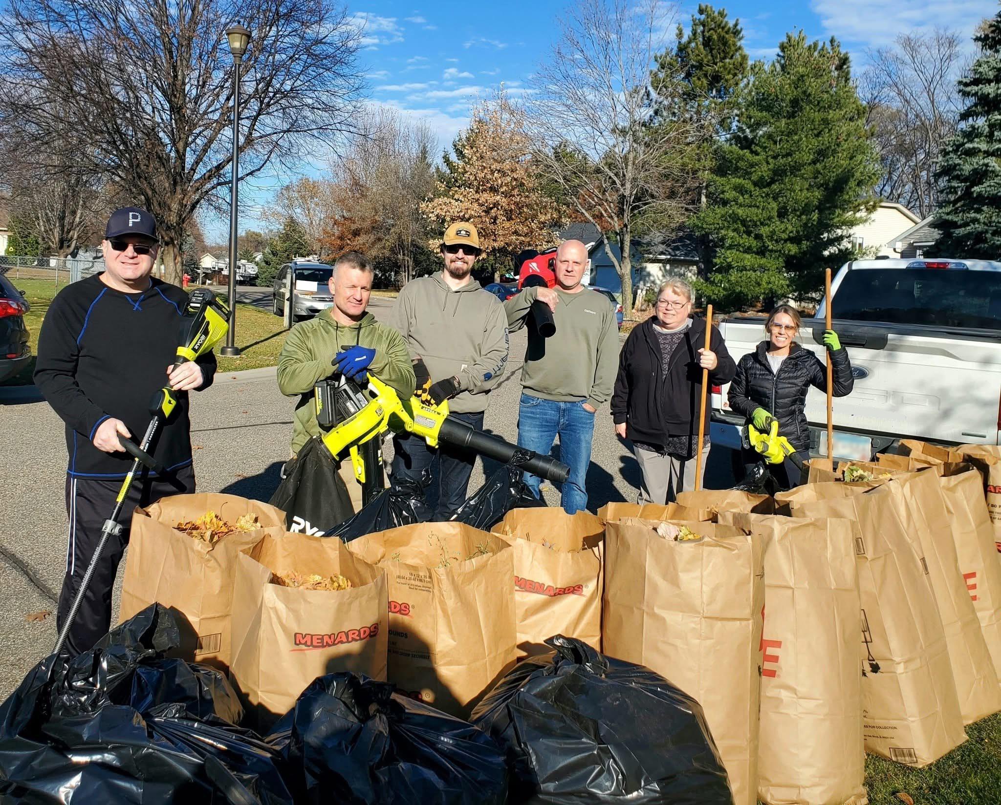 Volunteers with yard tools and bags of leaves after a cleanup.